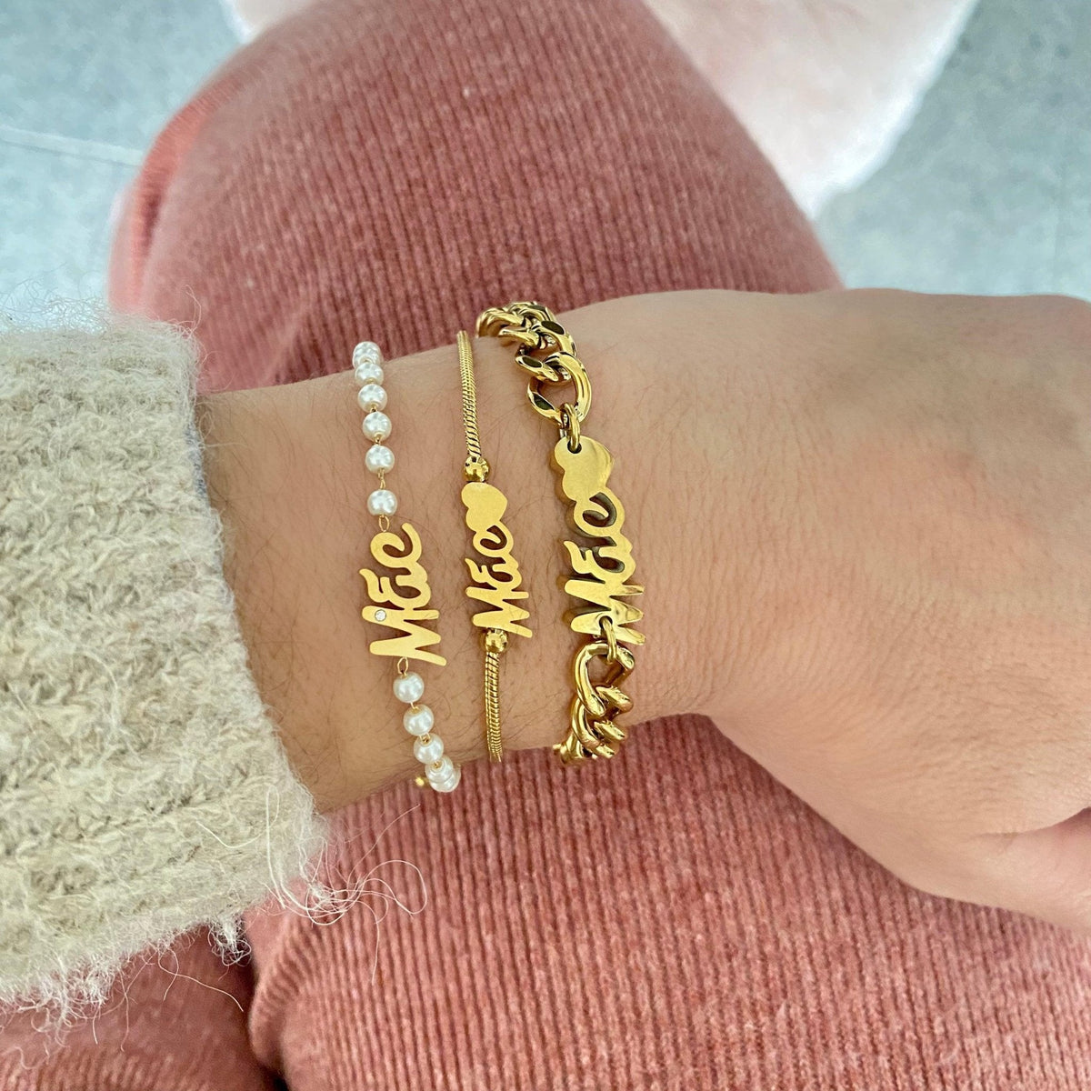 Conjunto de três pulseiras douradas GRINE com a palavra Mãe, incluindo uma com pérolas e uma de malha grossa.
