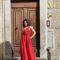 GRINE red cotton maxi dress with removable flower detail and spaghetti straps, worn by a model in front of a wooden door.
