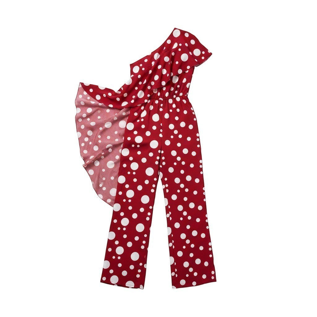 GRINE red and white polka dot one-shoulder jumpsuit with wide legs and elastic waist. Model wears sunglasses and holds a beaded bag.