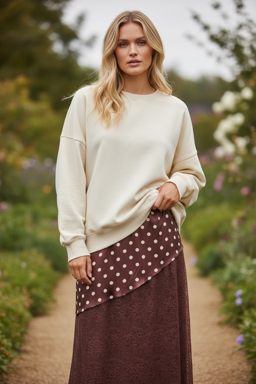 Modelo veste saia comprida GRINE cor chocolate com padrão de bolas e detalhes em renda, combinada com camisola bege
