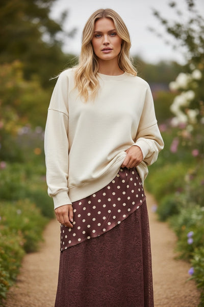 Modelo veste saia comprida GRINE cor chocolate com padrão de bolas e detalhes em renda, combinada com camisola bege