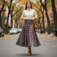 Modelo usa saia comprida GRINE com padrão xadrez, cintura subida e corte fluido em ambiente urbano de outono.