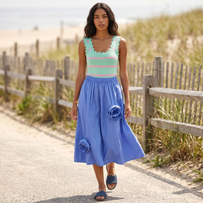Modelo veste saia midi GRINE azul com flores 3D em tecido técnico estruturado, combinada com top de alças em caminho de praia.