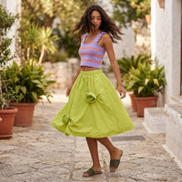 Modelo veste saia midi GRINE verde lima com flores 3D em tecido técnico estruturado num cenário de rua mediterrânica.