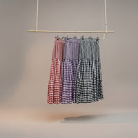Saia midi GRINE com padrão vichy em camadas, disponível em vermelho, roxo e preto. Cintura elástica e corte fluido.
