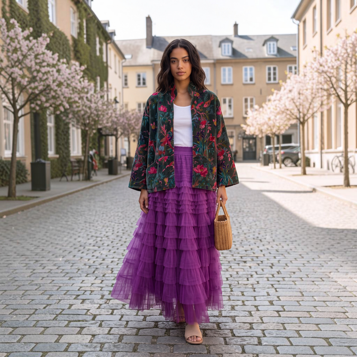 Modelo veste saia comprida de tule GRINE em rosa escuro com camadas, combinada com casaco estampado e mala de vime.