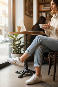 Mulher sentada num café usando sapatilhas GRINE Aura brancas com detalhe de estrela lateral e sola antiderrapante