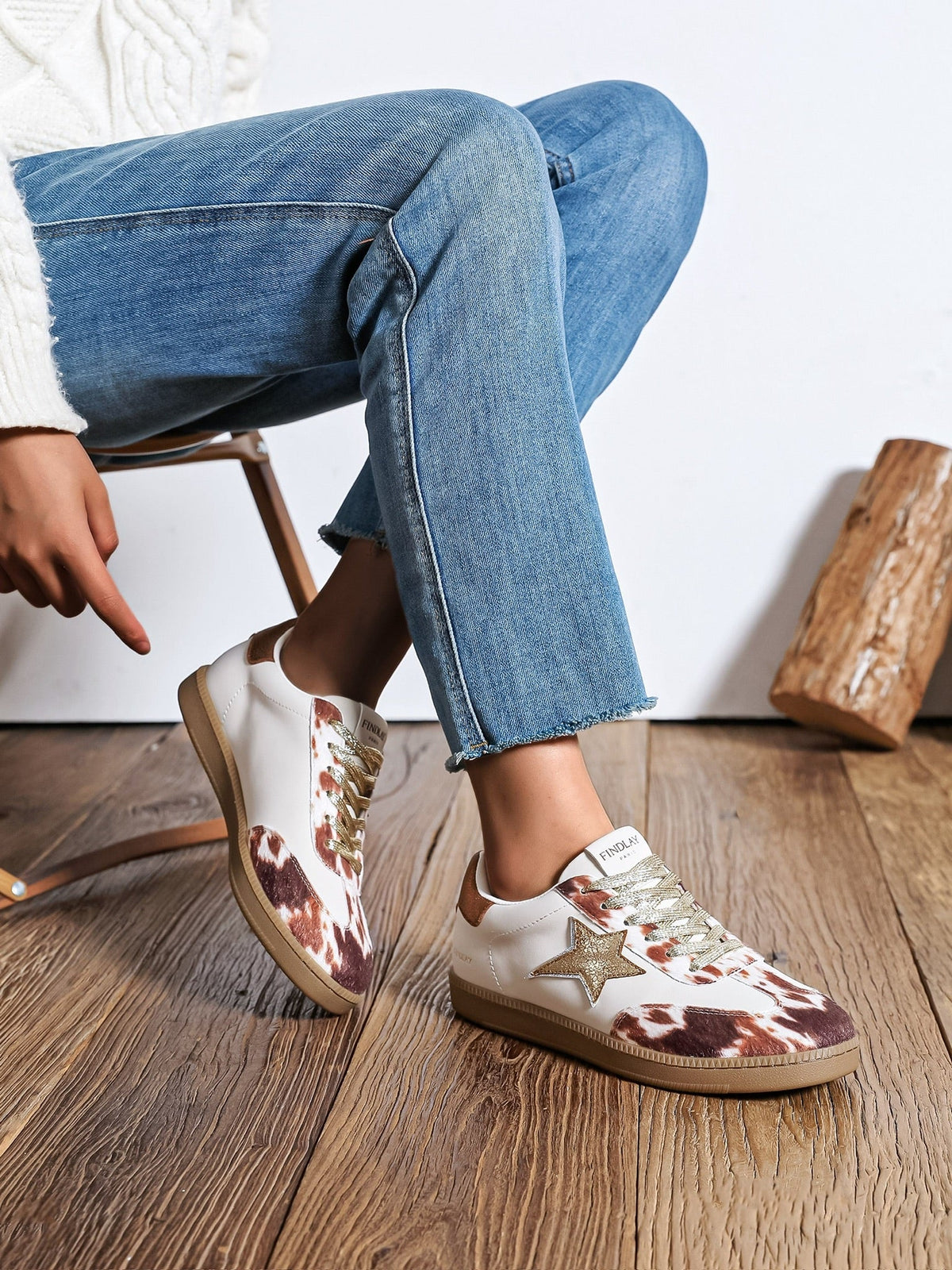 Sapatilhas GRINE Star Cow com padrão animal print, detalhe de estrela dourada e atacadores, usadas com calças de ganga