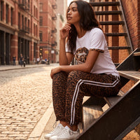 Modelo sentada em escadas de metal vestindo t-shirt branca GRINE com estampado de lábios em animal print e brilhantes