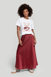 Modelo veste t-shirt branca de algodão GRINE com estampado de urso rosa, combinada com saia comprida acetinada bordô.