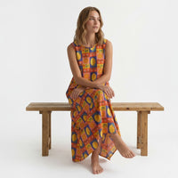 Modelo sentada num banco de madeira usando vestido GRINE comprido de algodão com padrão floral e citrinos multicolorido