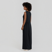 Modelo veste vestido comprido GRINE preto em algodão com corte evasê, decote redondo e sem mangas, vista lateral.