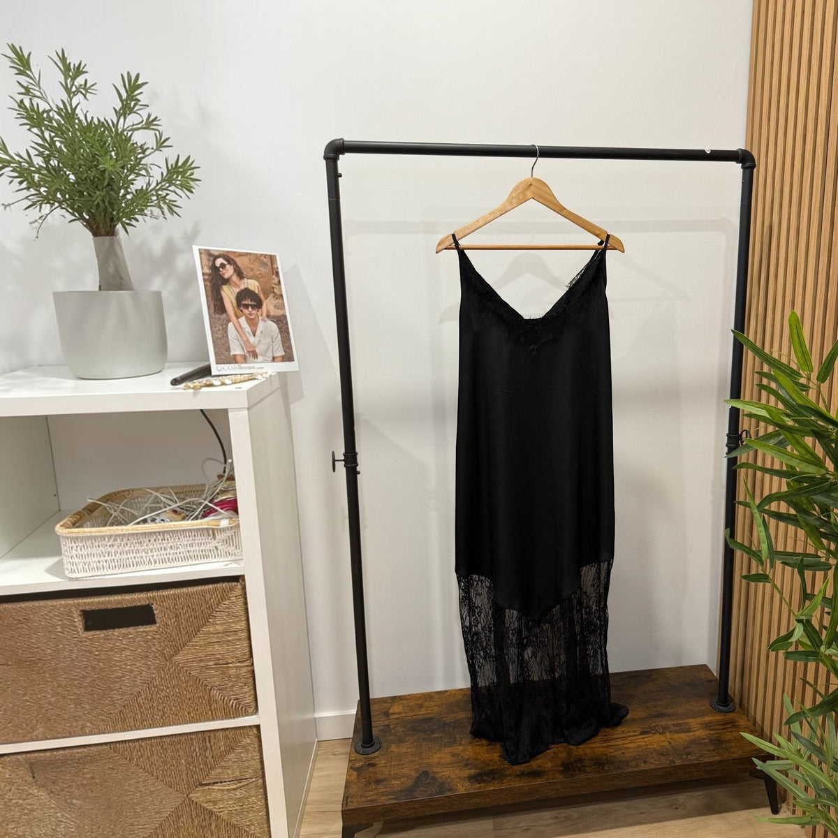 Vestido comprido preto GRINE com alças finas, decote e bainha em renda delicada num cabide de madeira.