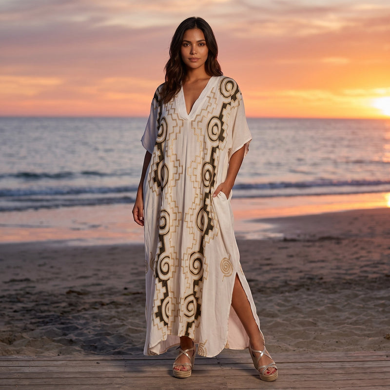 GRINE Vestido largo branco com padrão dourado e bolsos, decote em V e fendas laterais. Modelo veste tamanho M.