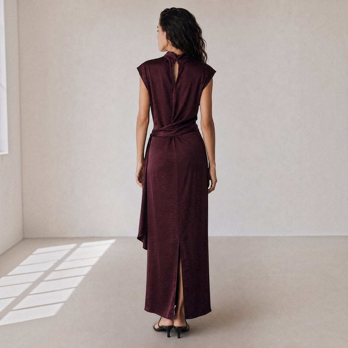 Vestido longo acetinado GRINE cor beringela com gola alta, sem mangas e faixa na cintura, visto de costas.